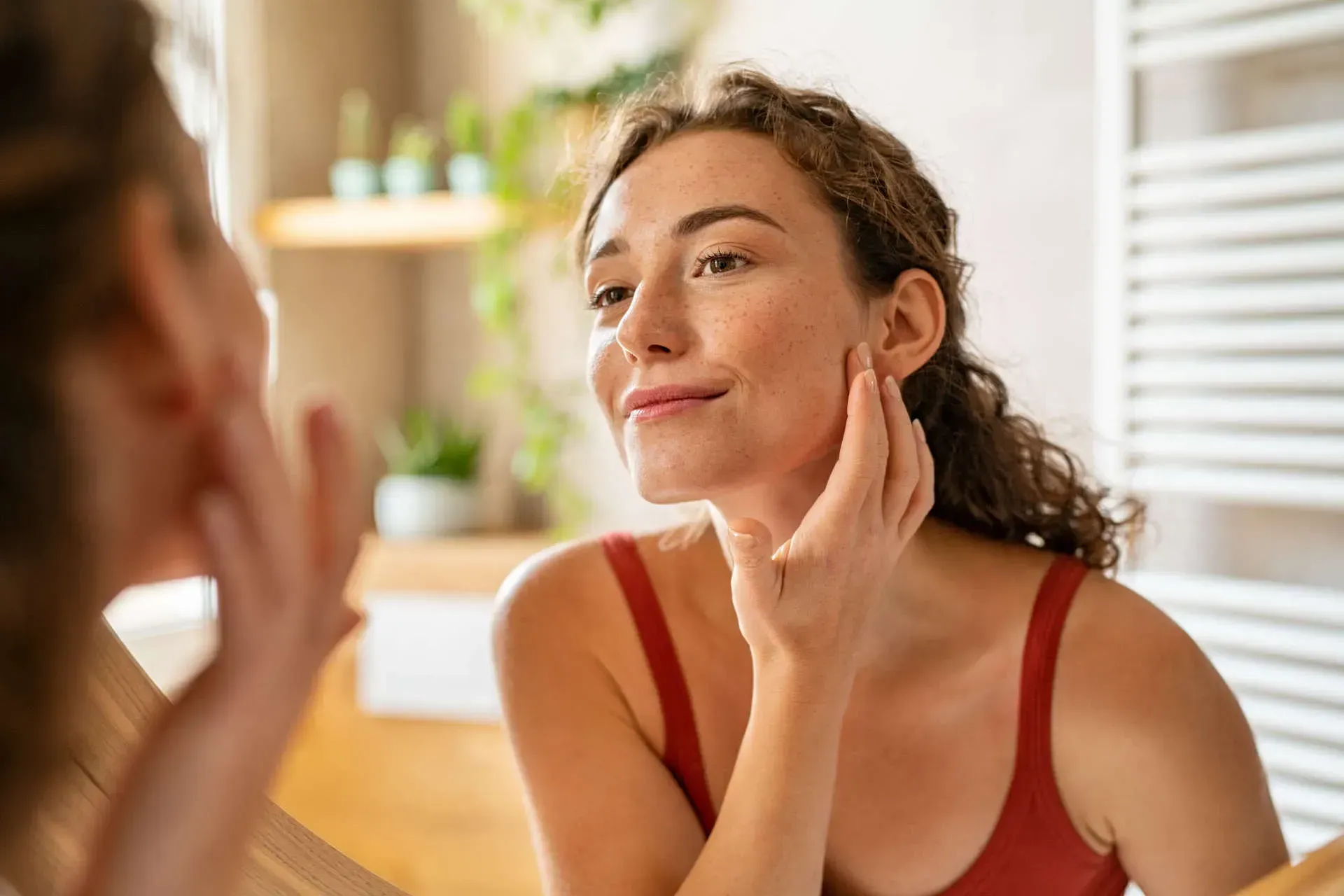 Woman applying skincare while looking in mirror.