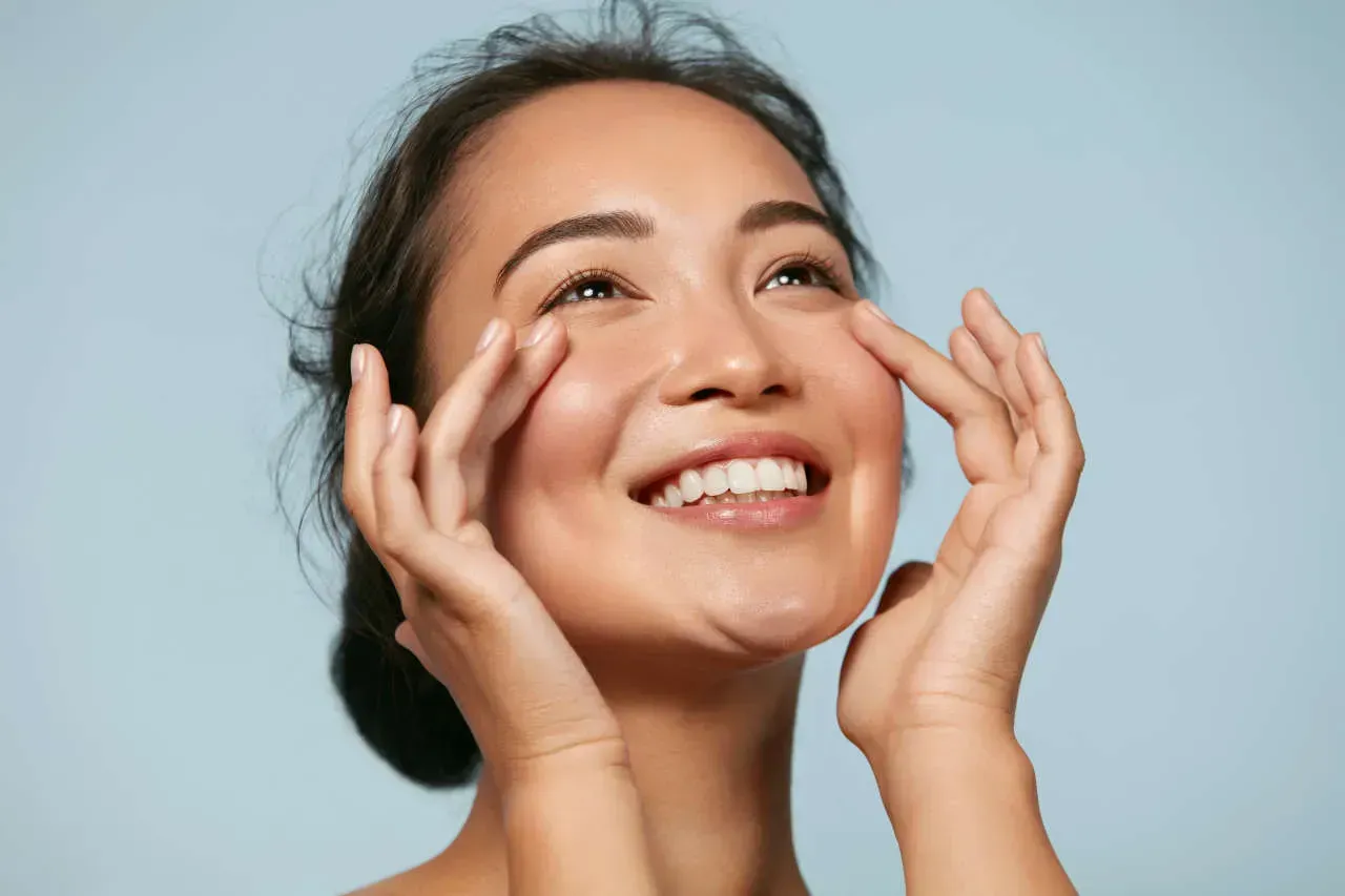 Woman smiling and applying facial skincare product.